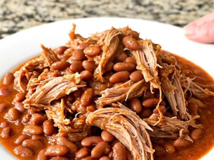 A slow cooker filled with a tender pork shoulder roast, pinto beans, and a flavorful red chili-tomato sauce.
