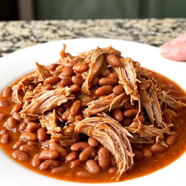 A slow cooker filled with a tender pork shoulder roast, pinto beans, and a flavorful red chili-tomato sauce.