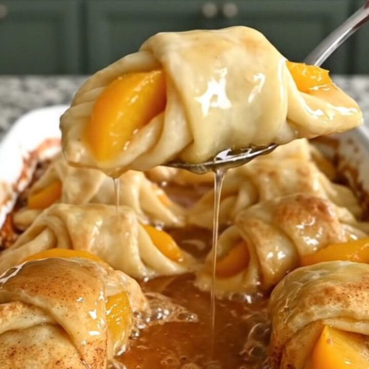 A ceramic baking dish filled with golden-brown peach crescent dumplings covered in a rich, bubbling cinnamon syrup.