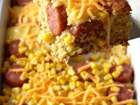A golden, freshly baked cornbread casserole with bubbling melted cheddar cheese and visible slices of smoked sausage.
