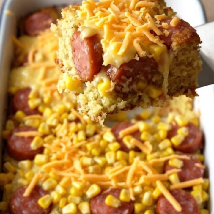 A golden, freshly baked cornbread casserole with bubbling melted cheddar cheese and visible slices of smoked sausage.