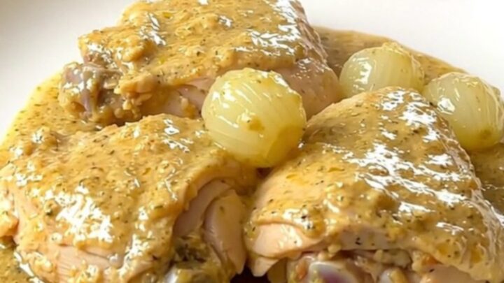 A slow cooker filled with cooked chicken thighs, whole pearl onions, and a rich, creamy white sauce with thyme.