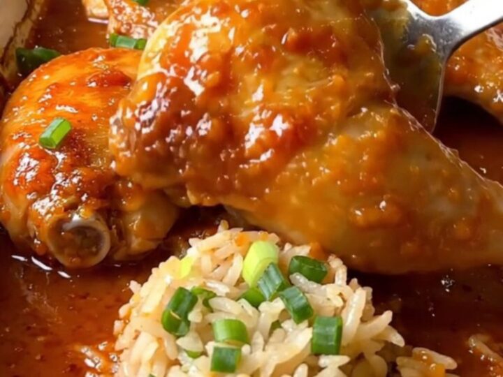 A top-down view of a rectangular baking dish filled with cooked chicken thighs, jasmine rice, and sweet chili sauce.