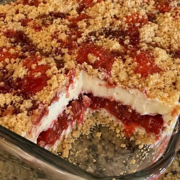 A golden-brown strawberry cheesecake dump cake in a glass dish with a serving removed.