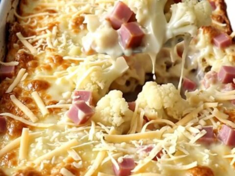 A top-down view of a rectangular white baker filled with cauliflower and ham in a creamy sauce, topped with Swiss cheese.
