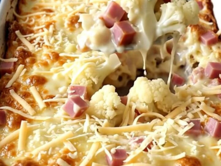 A top-down view of a rectangular white baker filled with cauliflower and ham in a creamy sauce, topped with Swiss cheese.