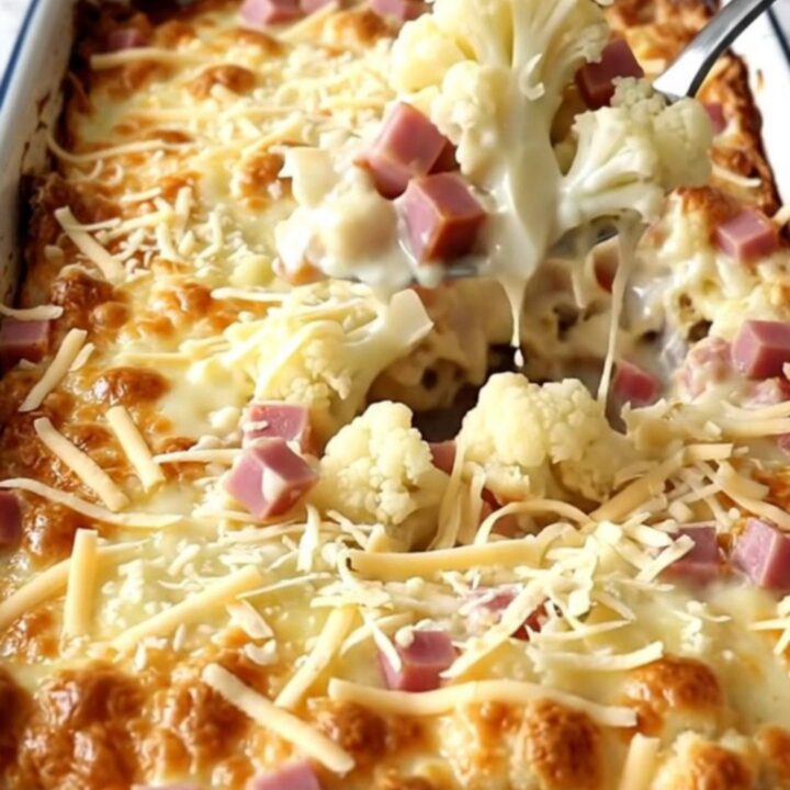 A top-down view of a rectangular white baker filled with cauliflower and ham in a creamy sauce, topped with Swiss cheese.