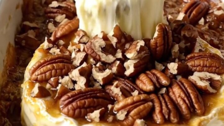 A warm, golden wheel of baked Brie in a white ceramic dish topped with caramelized brown sugar and toasted pecans.