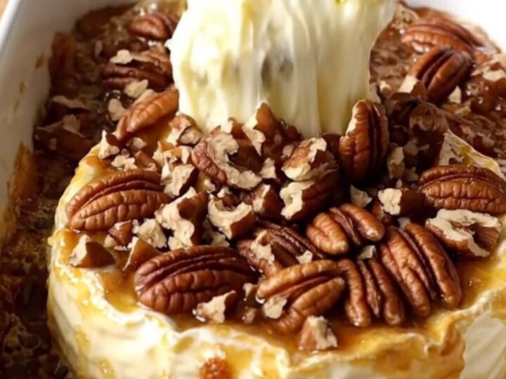 A warm, golden wheel of baked Brie in a white ceramic dish topped with caramelized brown sugar and toasted pecans.