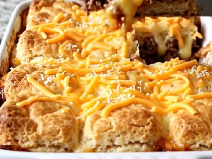 A golden-brown BBQ Bacon Burger Biscuit Bake in a white ceramic dish, featuring melted cheese and biscuits.