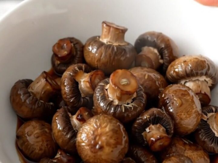A shallow white bowl filled with dark, wine-braised button mushrooms in a glossy, rich brown buttery sauce.