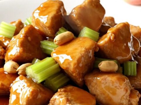 A white oval slow cooker filled with honey-glazed chicken cubes, roasted peanuts, and sliced celery.