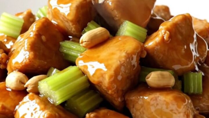 A white oval slow cooker filled with honey-glazed chicken cubes, roasted peanuts, and sliced celery.