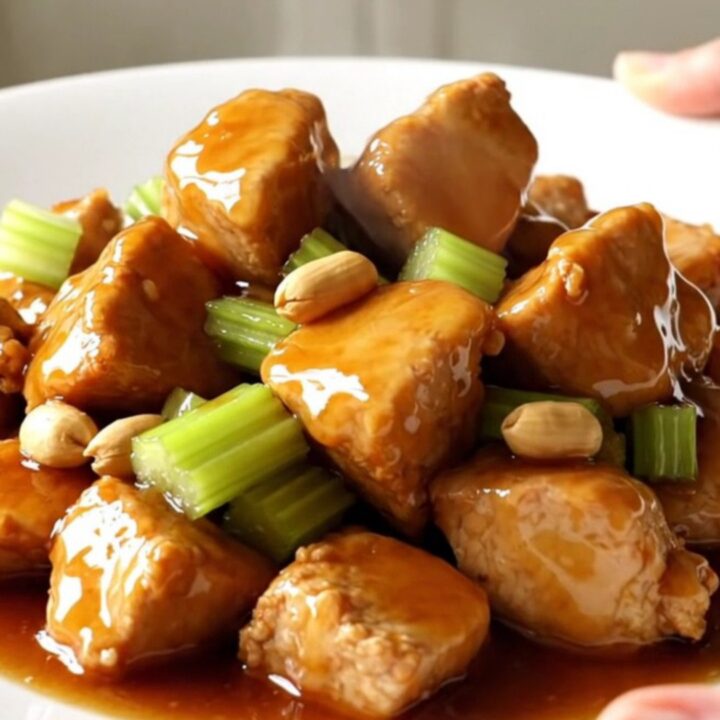 A white oval slow cooker filled with honey-glazed chicken cubes, roasted peanuts, and sliced celery.