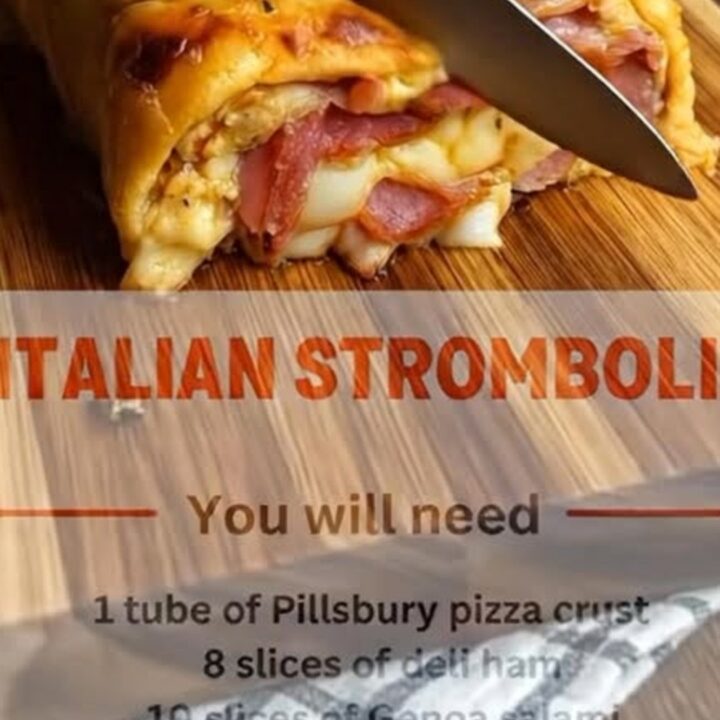 A golden-brown baked stromboli sliced on a wooden board, revealing layers of ham, salami, and melted cheese.