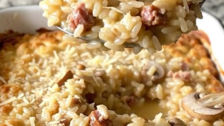 A large white baker filled with creamy, golden-brown baked risotto topped with sausage and mushrooms.