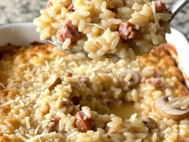 A large white baker filled with creamy, golden-brown baked risotto topped with sausage and mushrooms.