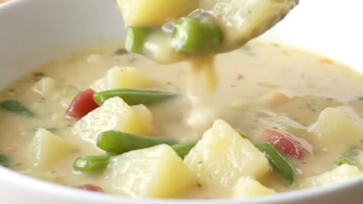 A creamy potato and green bean chowder in a white slow cooker insert on a light butcher-block counter.