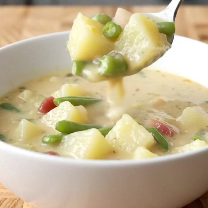 A creamy potato and green bean chowder in a white slow cooker insert on a light butcher-block counter.