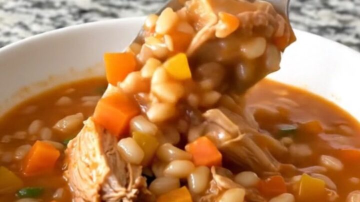 A steaming bowl of turkey and barley stew with visible pieces of carrot, green beans, and corn in a rich tomato broth.