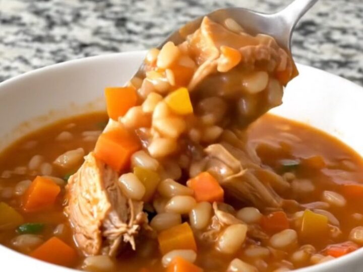 A steaming bowl of turkey and barley stew with visible pieces of carrot, green beans, and corn in a rich tomato broth.