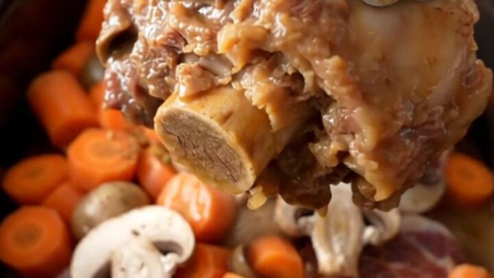 A close-up of tender bone-in beef shanks in a rich mushroom gravy with carrots in a slow cooker.