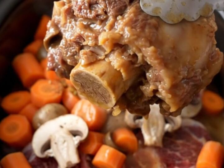 A close-up of tender bone-in beef shanks in a rich mushroom gravy with carrots in a slow cooker.