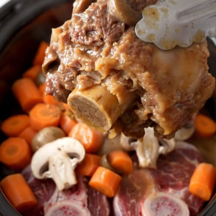 A close-up of tender bone-in beef shanks in a rich mushroom gravy with carrots in a slow cooker.