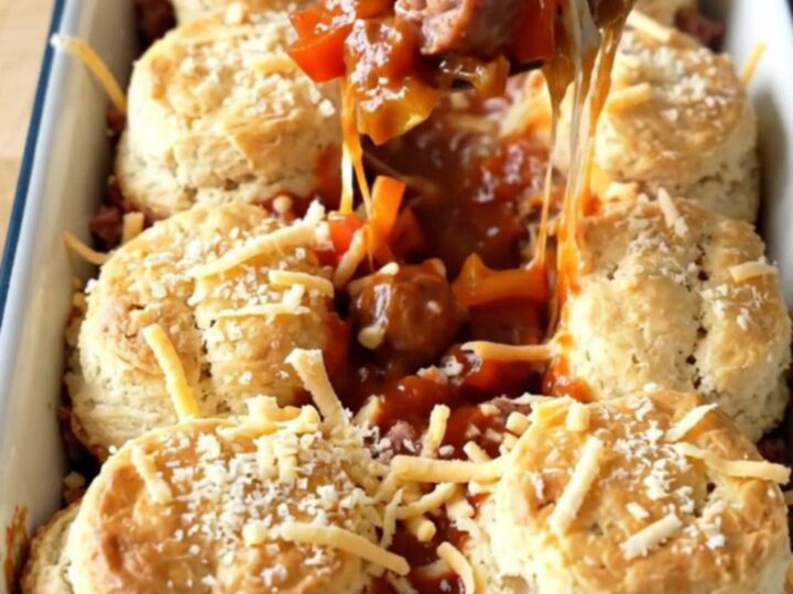 A golden, bubbling Italian sausage and pepper biscuit bake in a white rectangular baker on a butcher-block table.