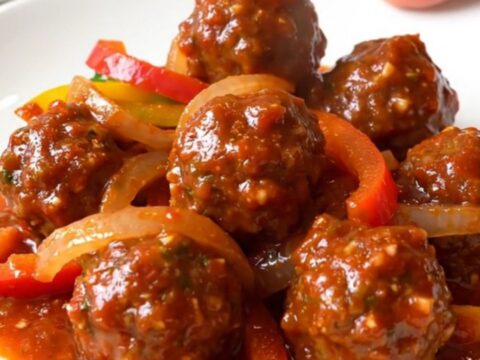 A close-up of tender chicken meatballs in a rich red salsa sauce with colorful bell pepper strips and onions in a slow