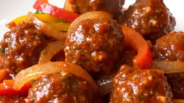 A close-up of tender chicken meatballs in a rich red salsa sauce with colorful bell pepper strips and onions in a slow