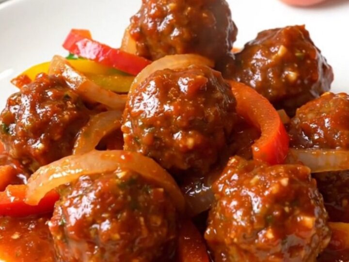 A close-up of tender chicken meatballs in a rich red salsa sauce with colorful bell pepper strips and onions in a slow