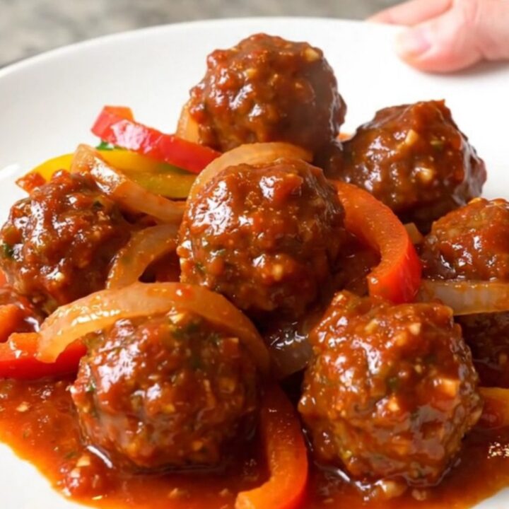 A close-up of tender chicken meatballs in a rich red salsa sauce with colorful bell pepper strips and onions in a slow