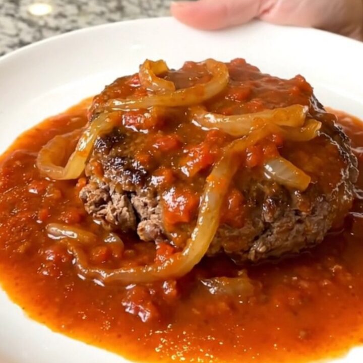 A rustic slow cooker filled with tender hamburger steaks smothered in a rich tomato and onion gravy.