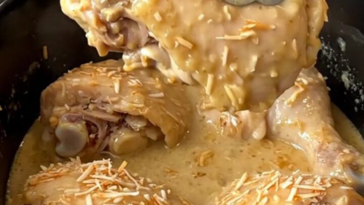 A close-up of tender, braised coconut chicken thighs covered in a creamy tan sauce in a black slow cooker.