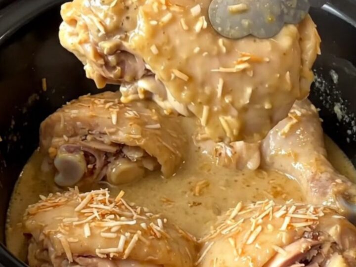A close-up of tender, braised coconut chicken thighs covered in a creamy tan sauce in a black slow cooker.