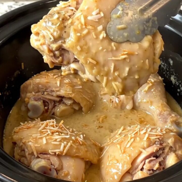 A close-up of tender, braised coconut chicken thighs covered in a creamy tan sauce in a black slow cooker.