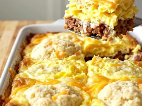 A golden-brown garlic cheddar biscuit breakfast bake in a white ceramic dish on a wood background.