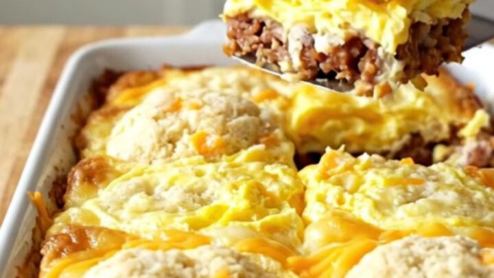 A golden-brown garlic cheddar biscuit breakfast bake in a white ceramic dish on a wood background.