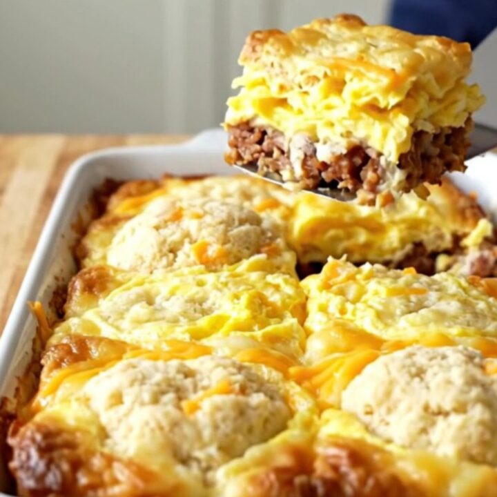 A golden-brown garlic cheddar biscuit breakfast bake in a white ceramic dish on a wood background.