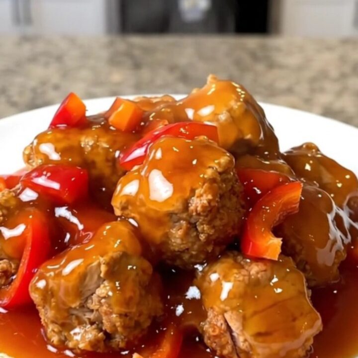 A close-up of tender turkey bites in a tangy red-orange sweet and sour sauce with pineapple and peppers.