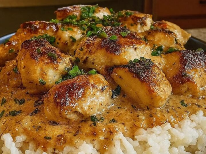 A dark bowl filled with fluffy white rice topped with golden seared chicken bites and a rich, creamy herb gravy.