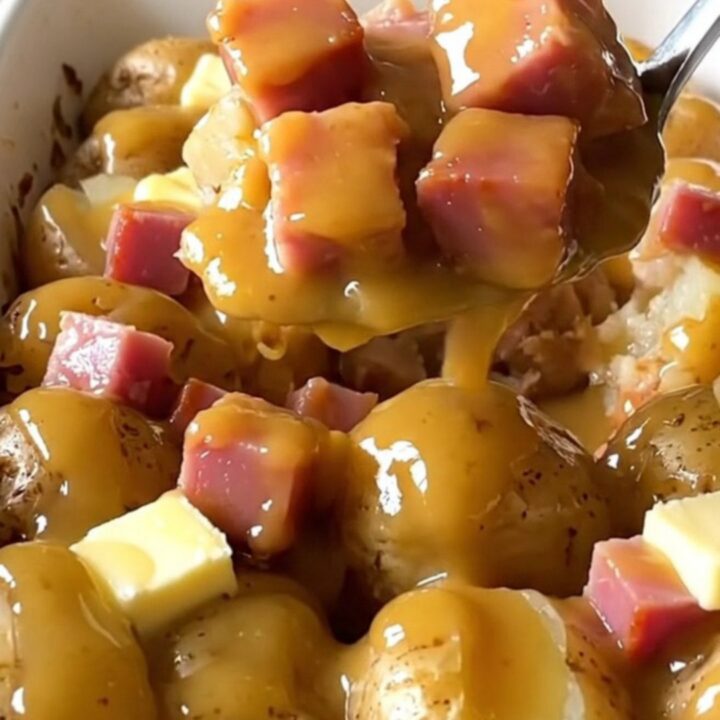 A top-down view of a ceramic baking dish filled with halved baby gold potatoes and cubed ham.