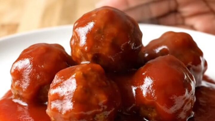 A close-up of tender, glazed party meatballs in a slow cooker, covered in a rich, shiny red sauce with visible onion bits.