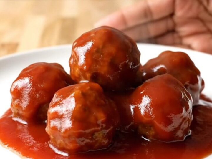 A close-up of tender, glazed party meatballs in a slow cooker, covered in a rich, shiny red sauce with visible onion bits.