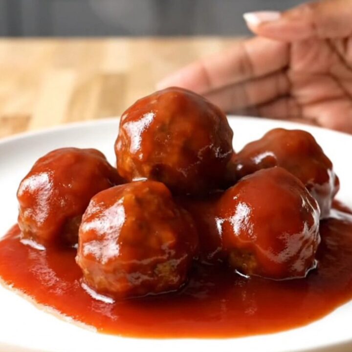 A close-up of tender, glazed party meatballs in a slow cooker, covered in a rich, shiny red sauce with visible onion bits.