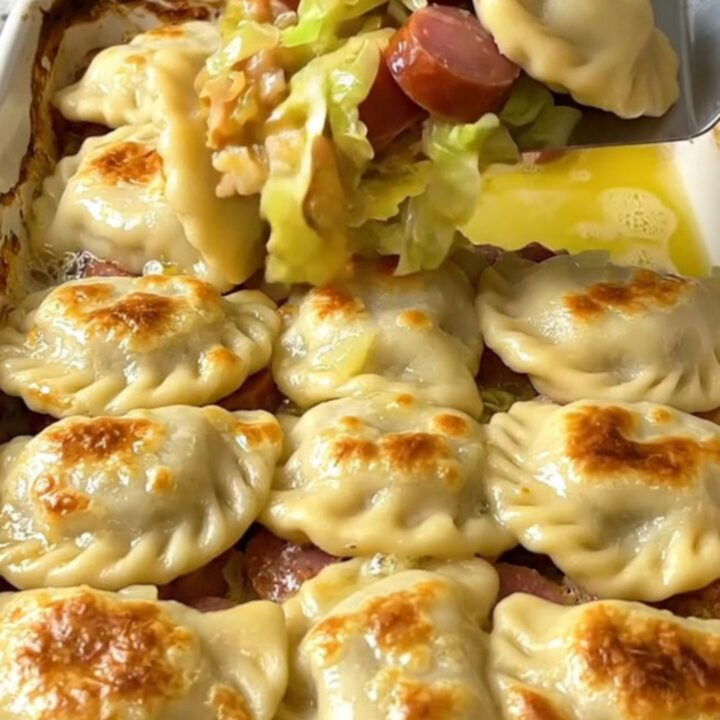 A golden, crispy pierogi-topped cabbage and kielbasa bake in a rectangular ceramic dish.