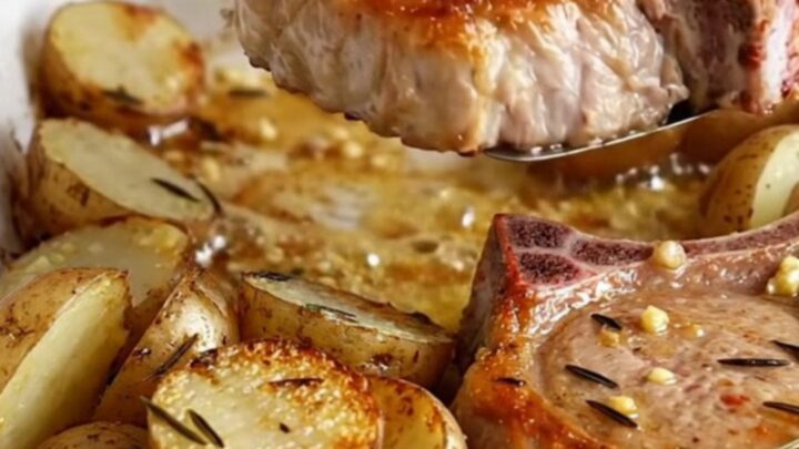 A rustic ceramic dish filled with golden-brown bone-in pork chops and roasted baby red potatoes with herbs.