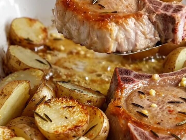 A rustic ceramic dish filled with golden-brown bone-in pork chops and roasted baby red potatoes with herbs.