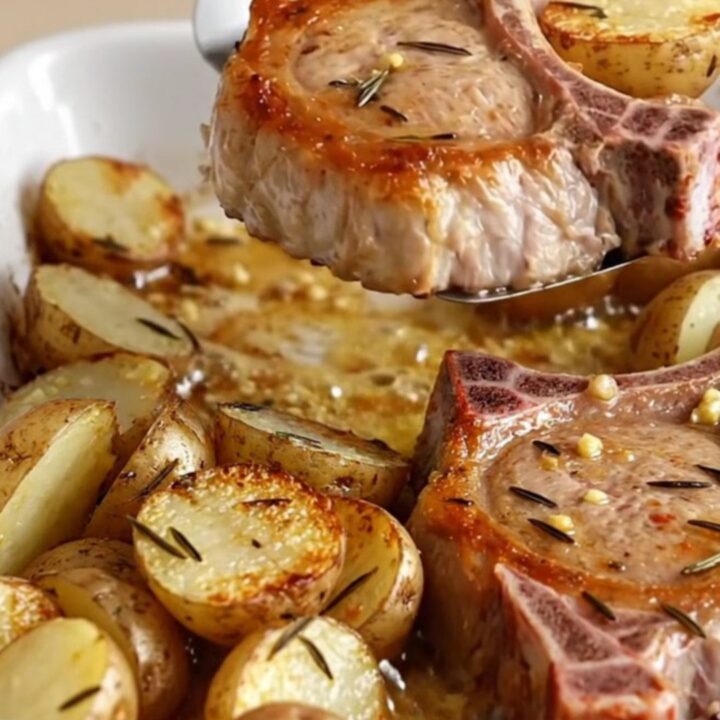 A rustic ceramic dish filled with golden-brown bone-in pork chops and roasted baby red potatoes with herbs.